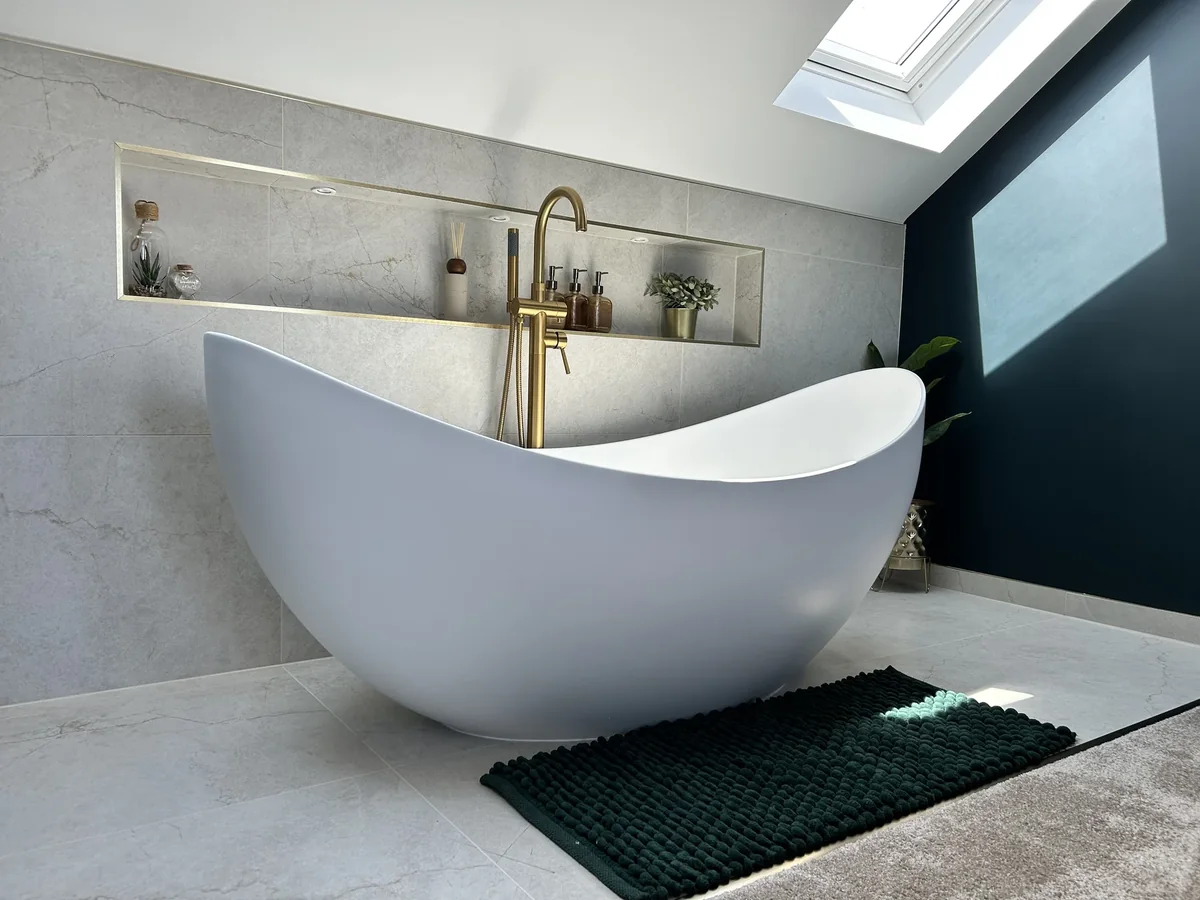 White freestanding bath beside a tiled wall and dark accent wall beneath a rooflight.
