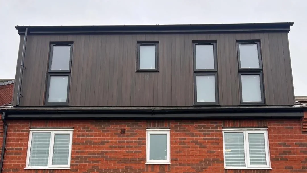 Dark clad dormer across the rear roof above a brick house.