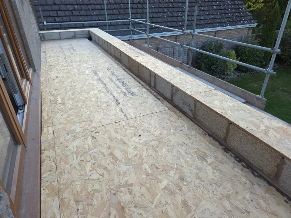 Boarded roof deck beside scaffolding and a low brick parapet.