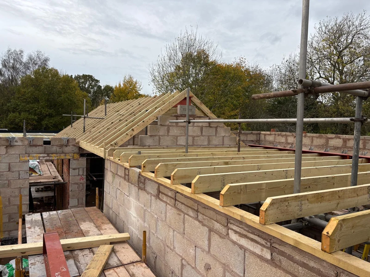 Timber roof trusses and joists resting on new block walls beside scaffolding.