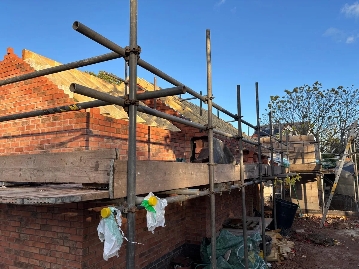 Close view of new brickwork meeting existing walls with scaffold tubes in front.
