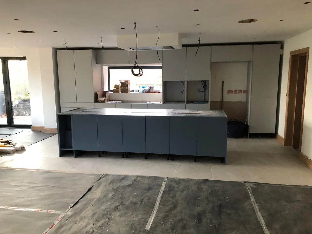 Grey kitchen units and an island being fitted in a large room.
