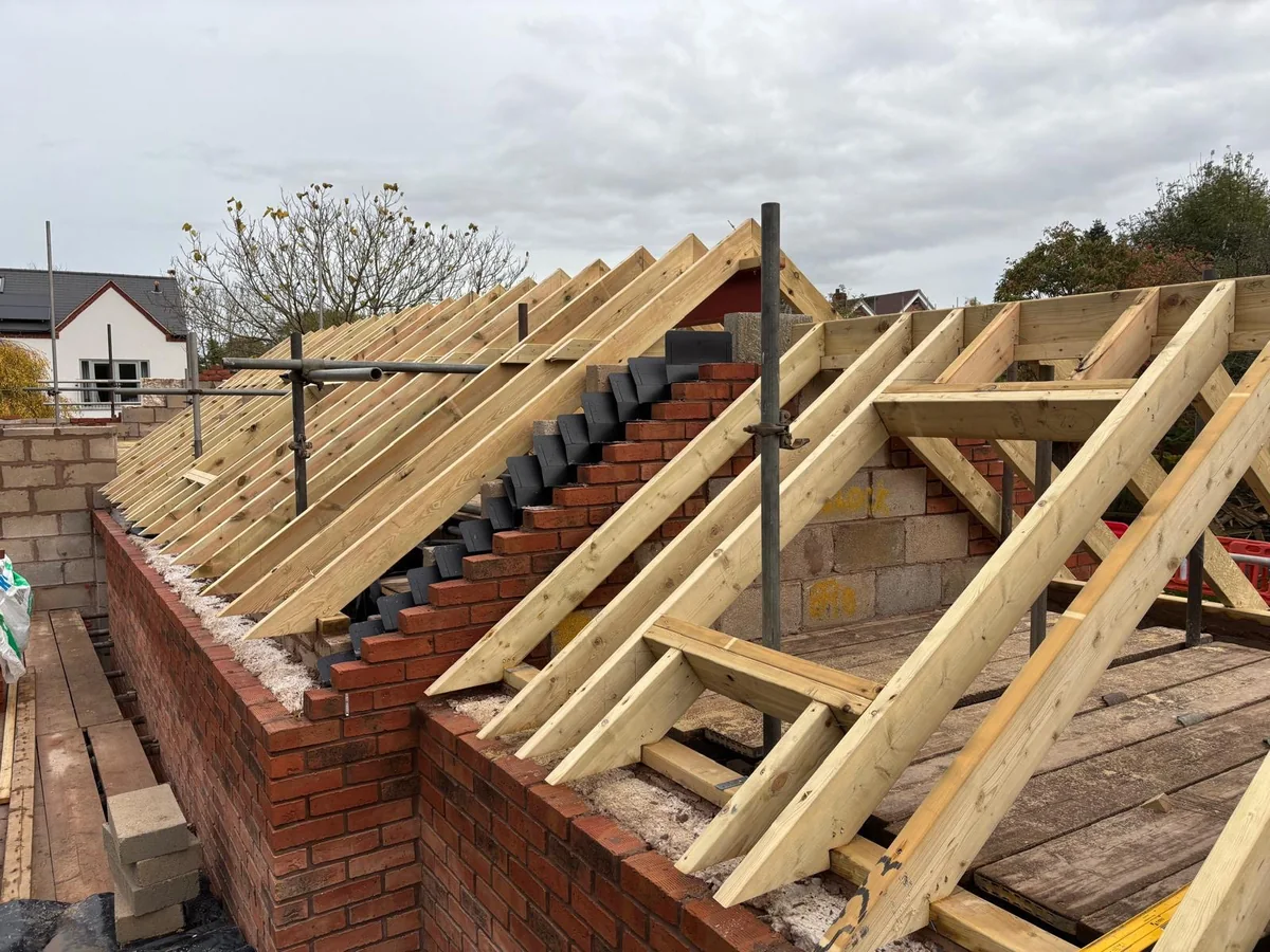 Pitched timber roof frame over an unfinished brick and block extension.