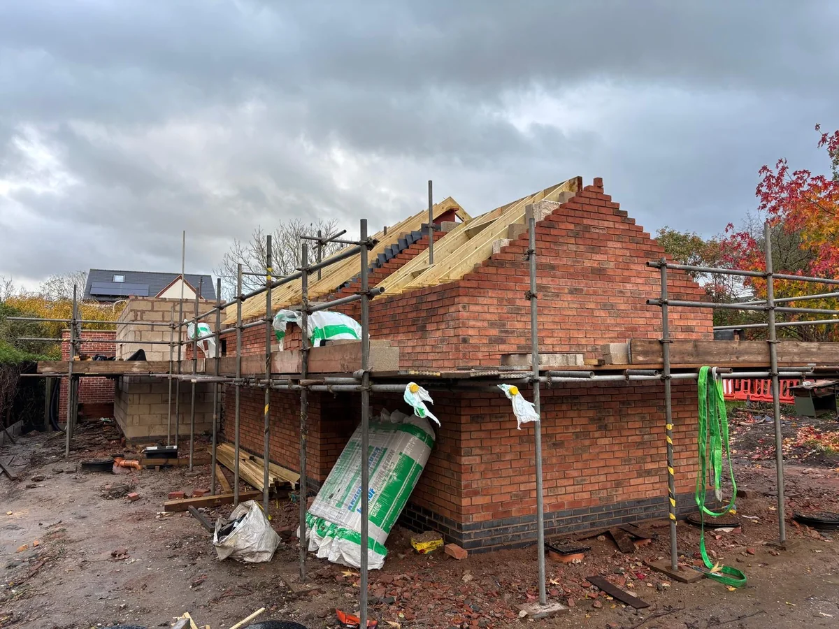 Scaffolded brick extension with a partly tiled pitched roof beside the existing house.