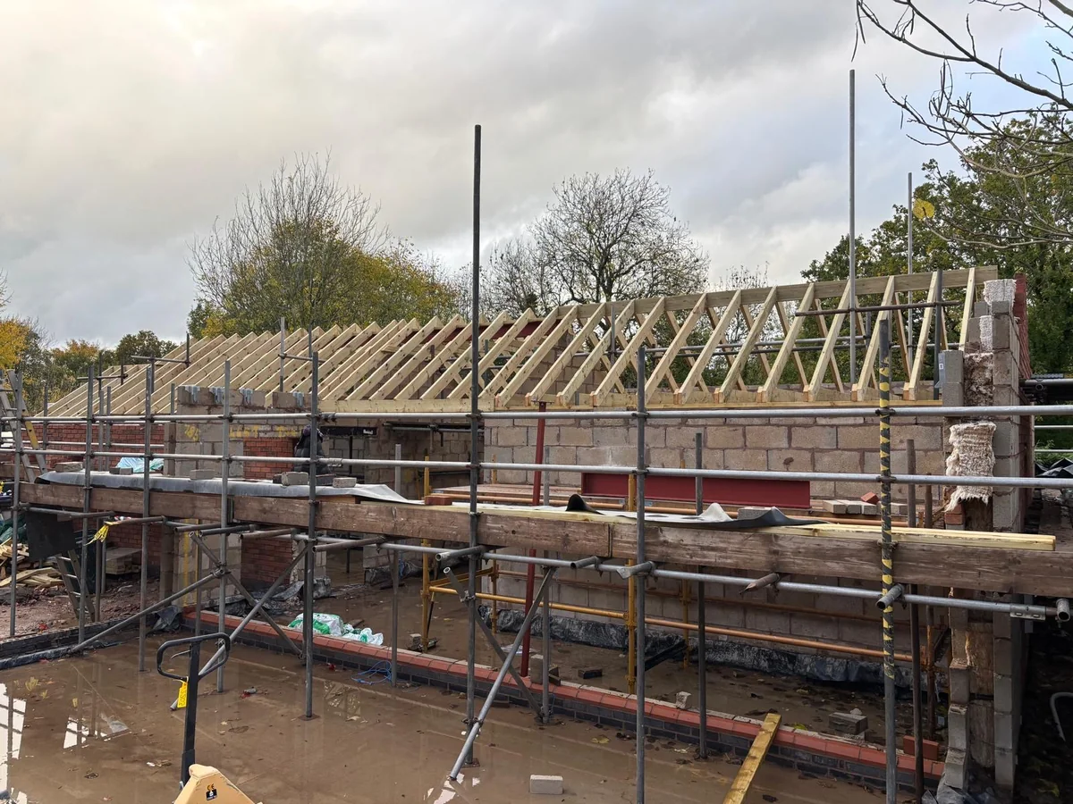 Roof trusses set across a long single storey brick extension inside scaffolding.