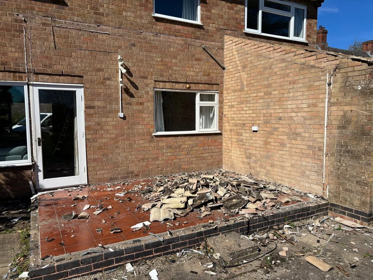 Rear brick wall with doors, window and rubble before new opening.