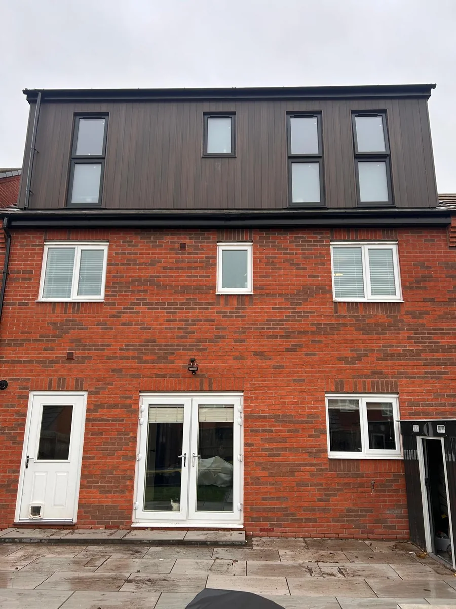 Dark clad rear dormer above a brick house with lower patio doors.
