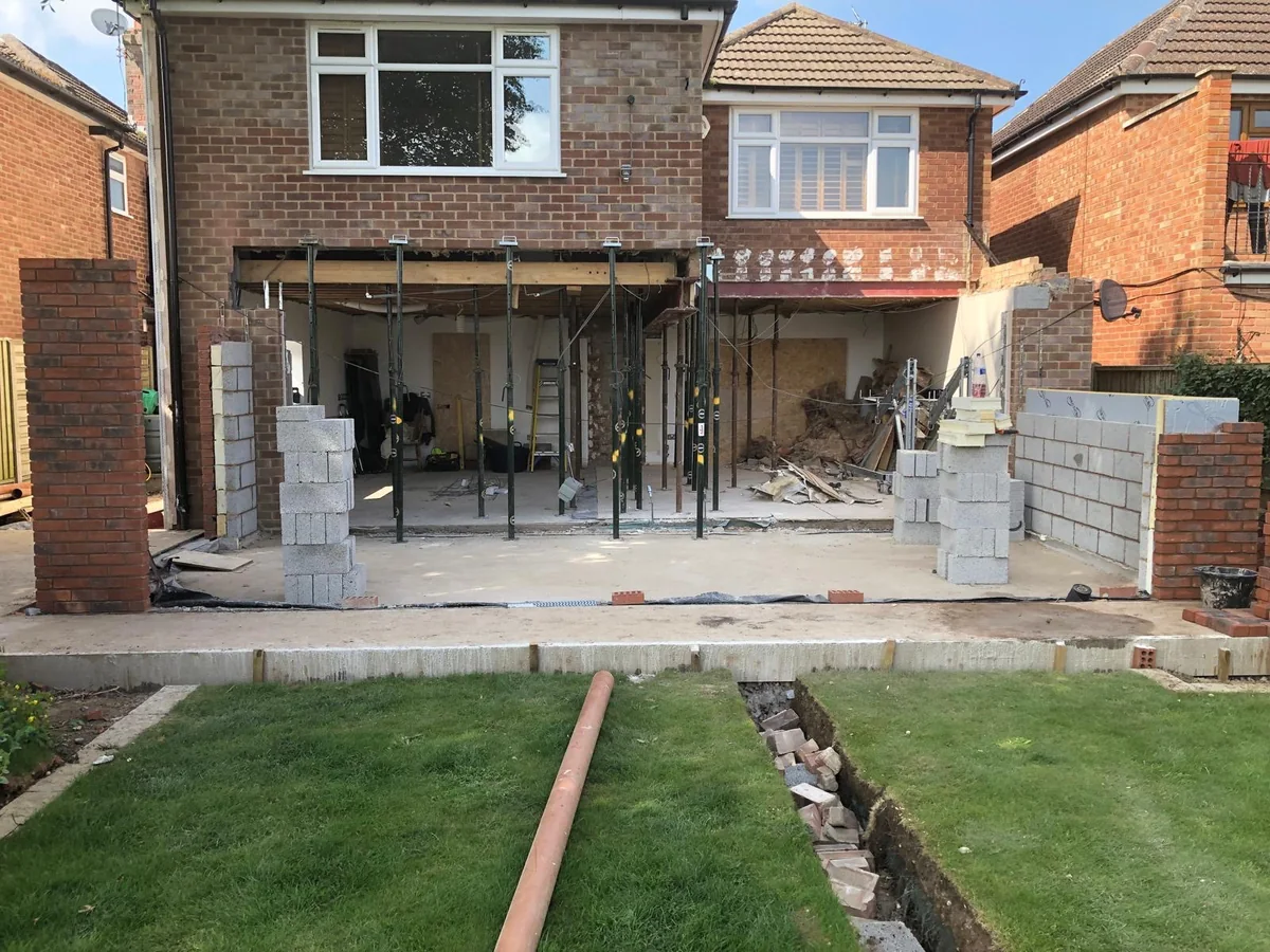 Temporary steel props supporting a wide opening under the brick upper storey of a house.