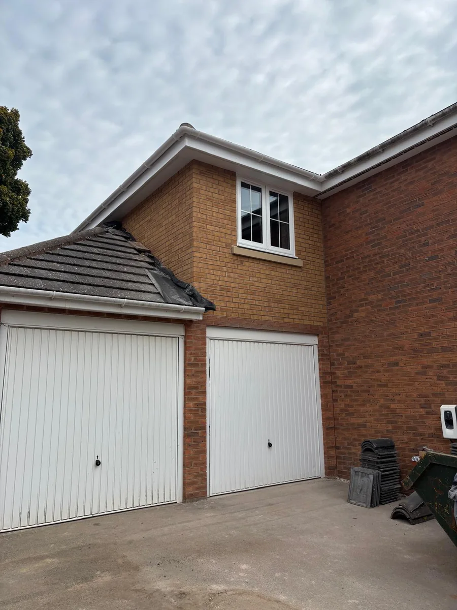 Two white garage doors beside a brick house.