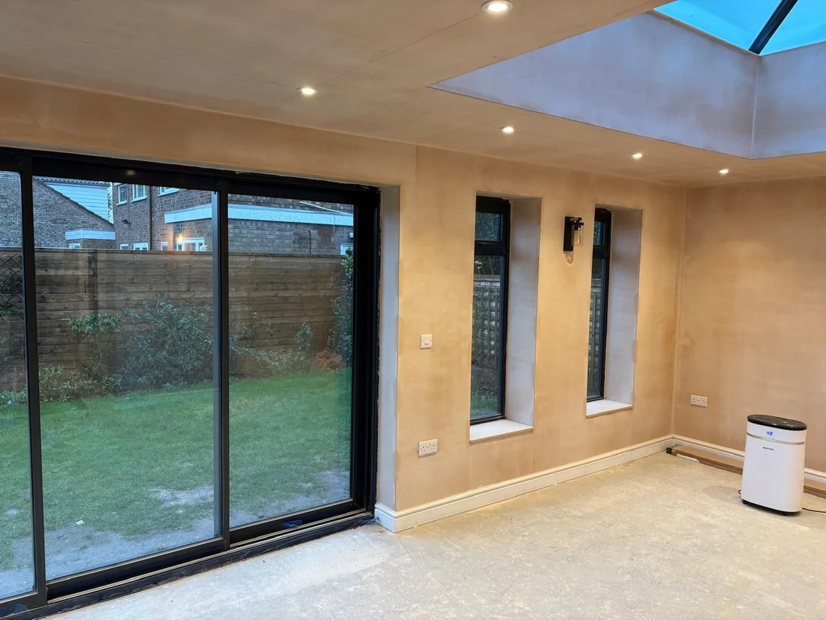 Finished room with roof lantern, narrow side windows and sliding doors to a garden.