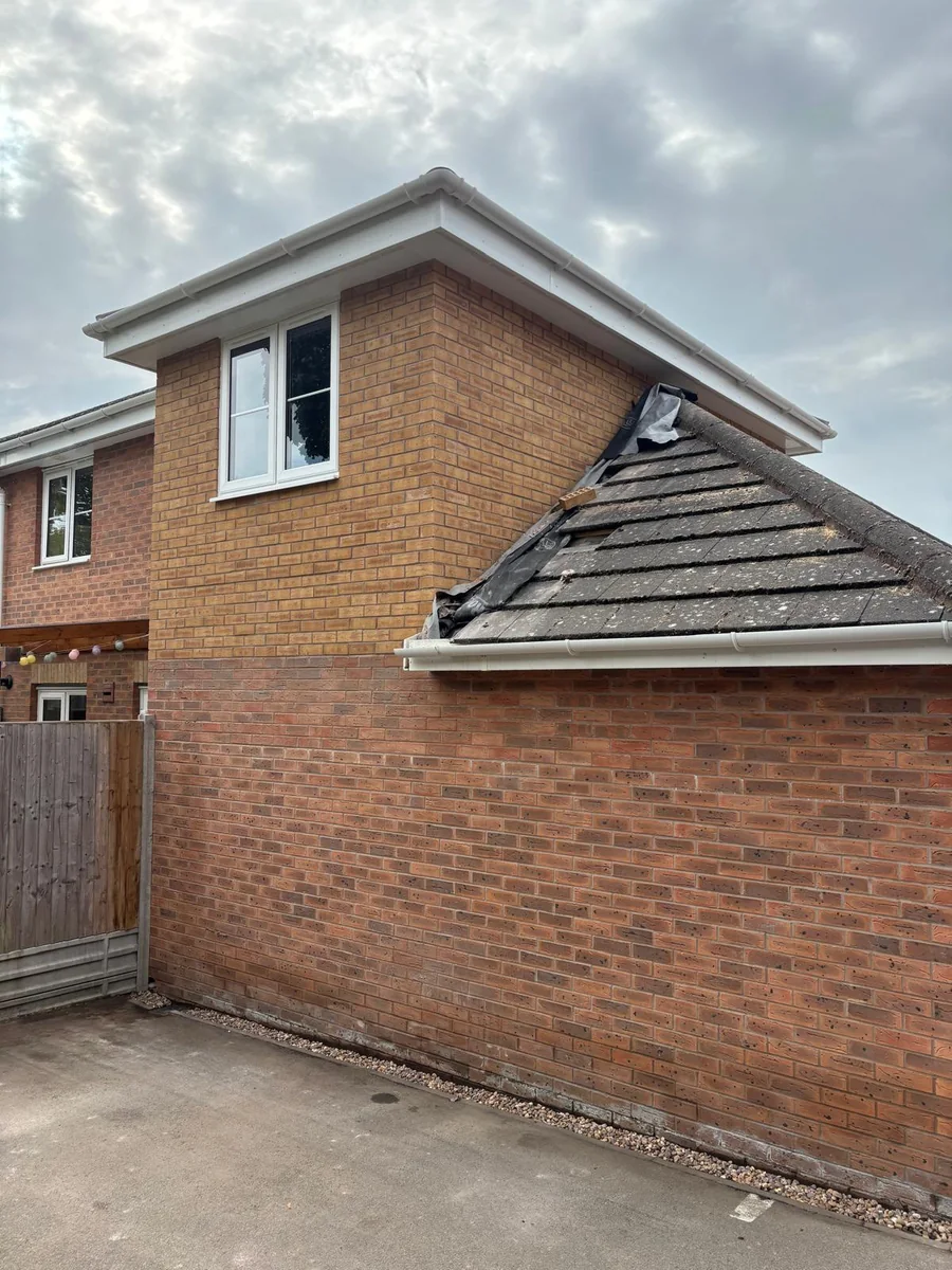 Brick side wall and pitched roof of a garage beside a house.