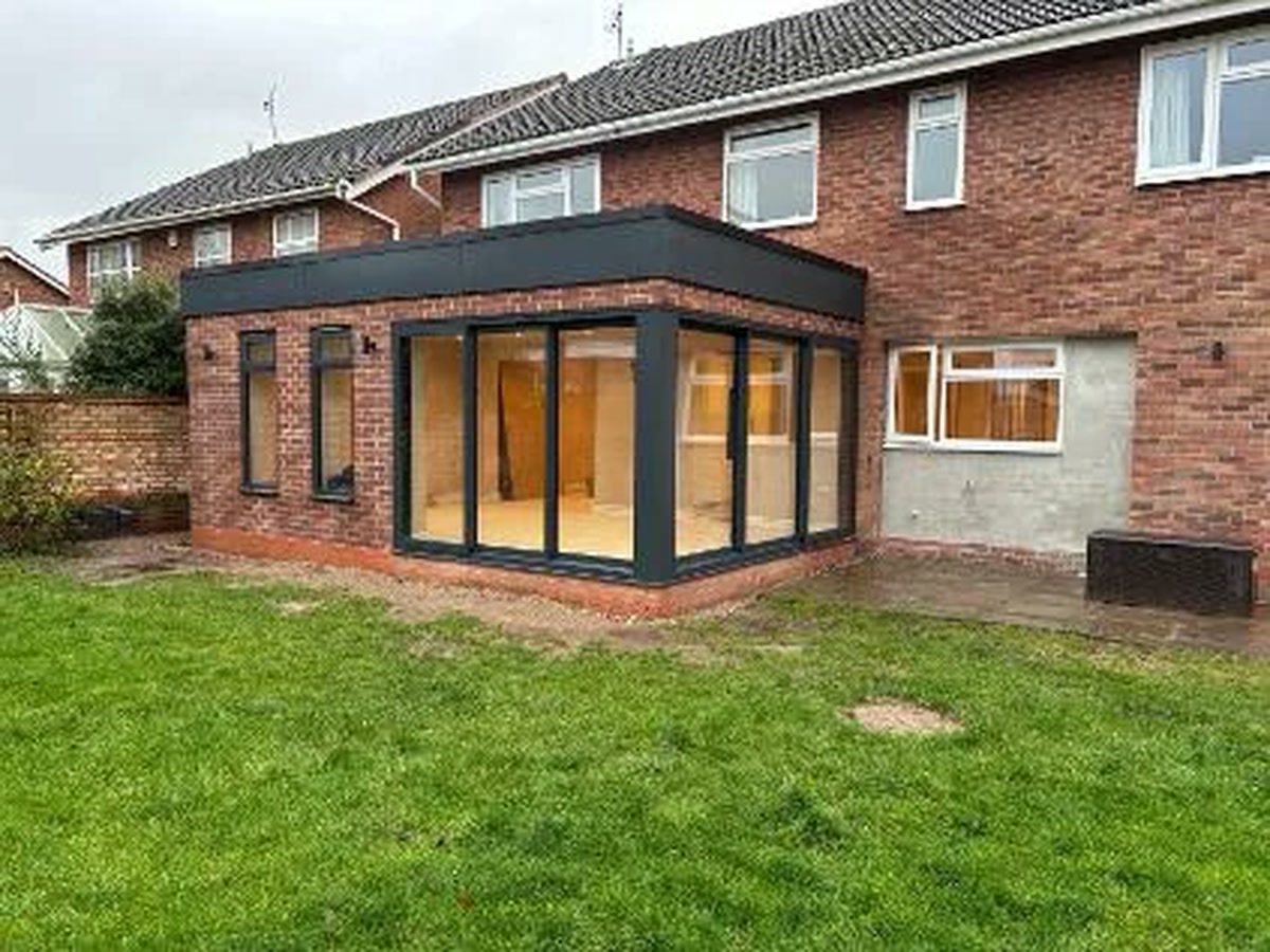 Single-storey brick rear extension with black framed glazing facing a lawn